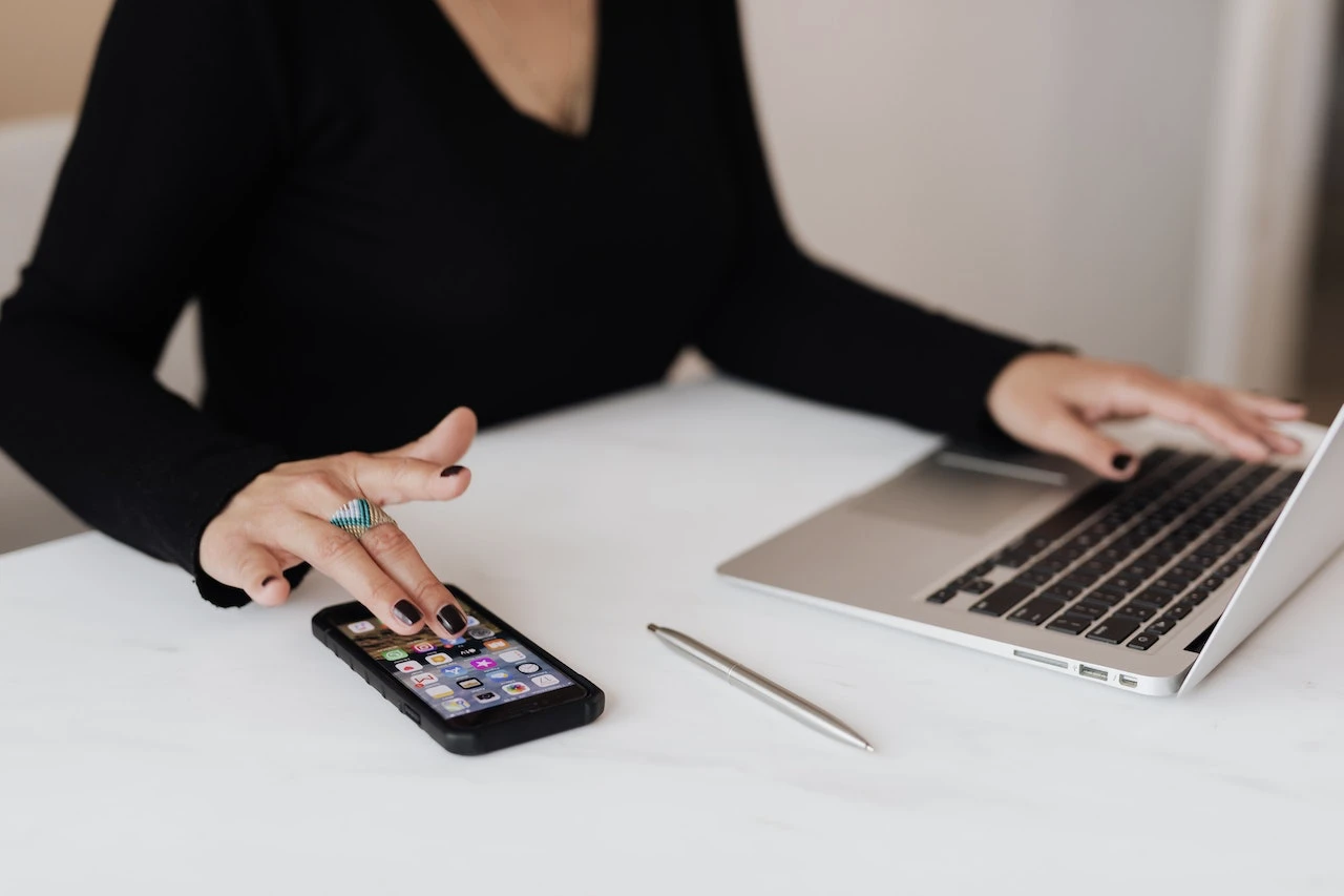A person working at a laptop while also working on a phone
